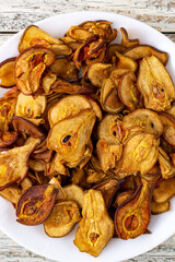 A pile of dried pears in slices on a white plate on wooden background. Dried fruit chips. Healthy food
