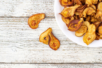A pile of dried pears in slices on a white plate on wooden background. Dried fruit chips. Healthy food