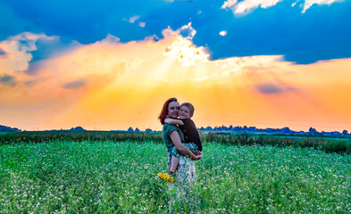 Fototapeta premium A woman and her son embrace against the background of the sunset