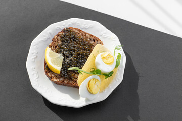 Black caviar on a festive sandwich with eggs, lemon, greenery. Healthy rich in antioxidants tasty...