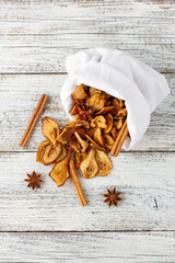 A pile of dried slices of pears and spices pills out of a white pouch on wooden background. Dried fruit chips.