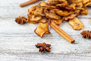 A pile of dried slices of pears and spices pills out of a white pouch on wooden background. Dried fruit chips.