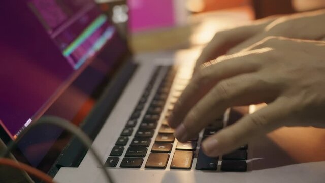 The hacker programmer starts working. A person stretches his fingers and turns on a computer program for writing code, against the background of monitors and a beautiful orange light. Close up.