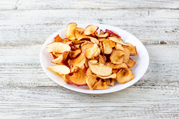 A pile of dried apples in slices on a white plate on wooden background. Dried fruit chips. Healthy food