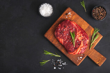 Raw rib eye steak of beef with rosemary on cutting board