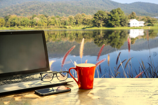 Red  Coffee Cup , Mobile Phone And Notbook Computer On Table In Morning With Nature Background At Sunrise,