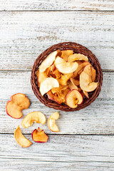 A pile of dried slices of apples in wicker basket on white wooden background. Dried fruit chips. Healthy food
