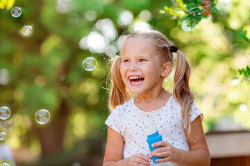  funny little blonde girl blowing soap bubbles in summer in the park