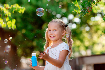funny funny little blonde girl blowing soap bubbles in summer in the park