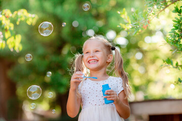 funny funny little blonde girl blowing soap bubbles in summer in the park