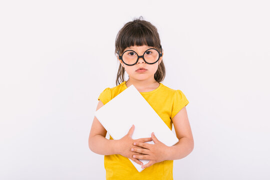 Small girl with serious gesture wearing yellow t-shirt and round black glasses holding a white paper in her hands on white background