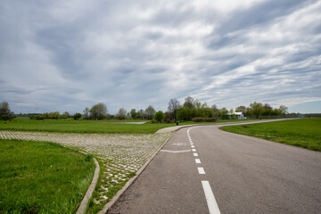 An asphalt road with markings goes away to the horizon. Low section shot, overcast weather, and low clouds in the background. Countryside, rural scenery, transportation, landscapes.