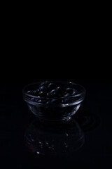 a handful of blueberries in a glass bowl on a black background