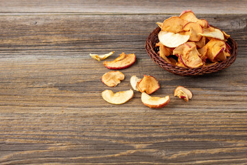 A pile of dried slices of apples in wicker basket on wooden background. Dried fruit chips. Healthy food