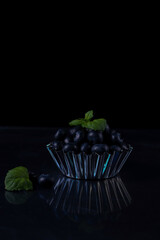 a handful of blueberries in a metal bowl on a black background.