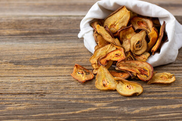 A pile of dried slices of pears pills out of a white pouch on wooden background. Dried fruit chips. Healthy food