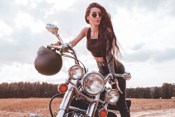 Sexy girl in a leather suit posing near a motorcycle at sunset. Travel concept.