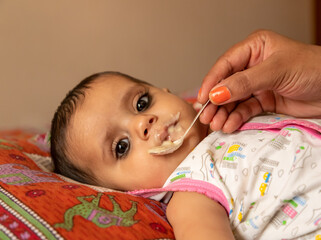 portrait of adorable indian baby girl eating porridge with spoon.