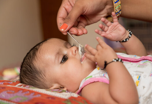 portrait of adorable indian baby girl eating porridge with spoon.