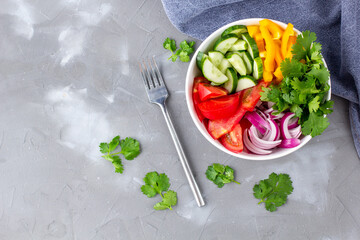 Plate of rainbow salad with different vegetables and herbs in white bowl on grey stone background