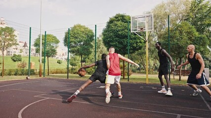 Group of multiracial young people playing basketball on court at outdoors. Professional sports. Team of millennial sportsmen engaged in basketball game at outdoor court in summer - Powered by Adobe