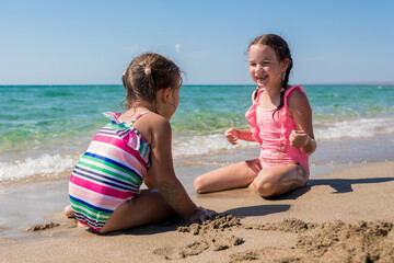 Summer time concept. Two adorable girls having fun on the beach. Children playing with sand. Family vacation at sea with kids. Summertime concept