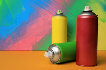 Cans of different spray paints on color background, space for text. Graffiti supplies