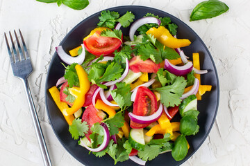Plate of rainbow salad with different vegetables and herbs on black plate on white stone background