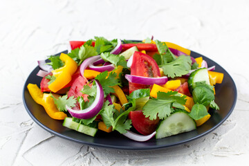Plate of rainbow salad with different vegetables and herbs on black plate on white background