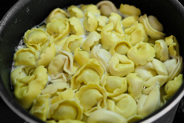 Tasty ravioli are boiled in a black saucepan. Homemade Italian cuisine. 