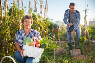 Portrait of elderly woman posing with basket full of harvested vegetables and greens at smallholding