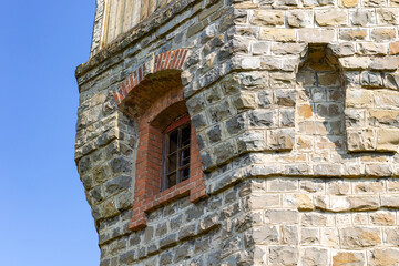 The upper part of an ancient watchtower made of stone blocks and wood paneling with windows against the blue sky on a bright sunny summer day. Close-up