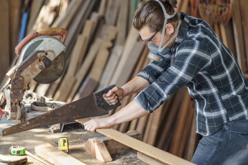 carpenter using saw hand cutting wooden plank in workshop . Young man builder sawing board ....