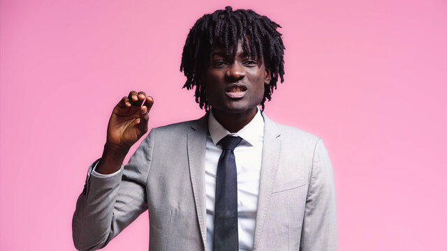 Skeptical african american businessman gesturing isolated on pink