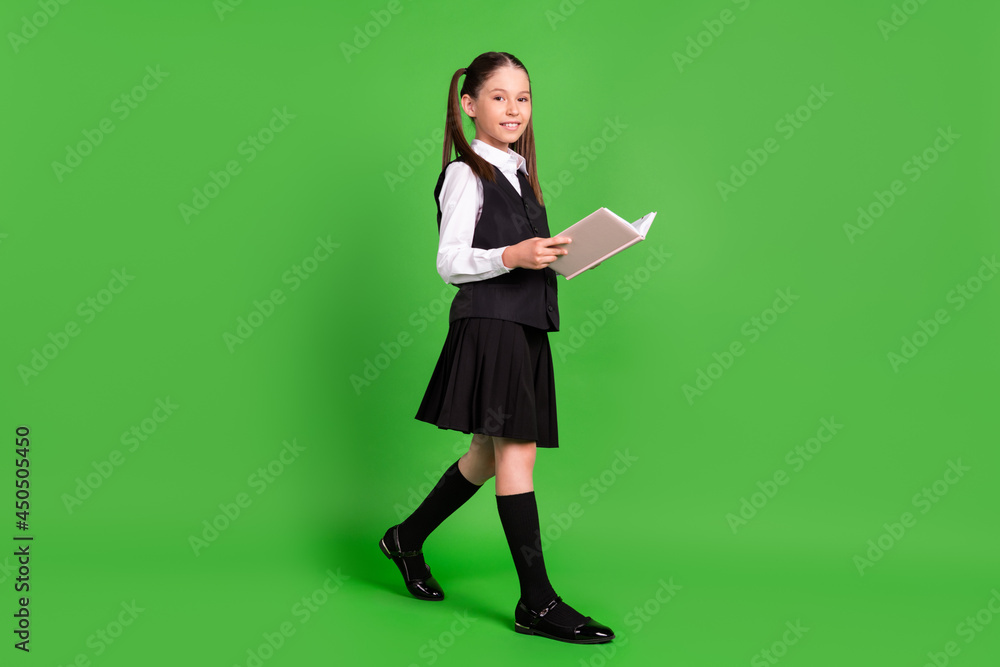 Wall mural Photo of charming pretty school girl wear black white uniform walking reading book smiling isolated green color background