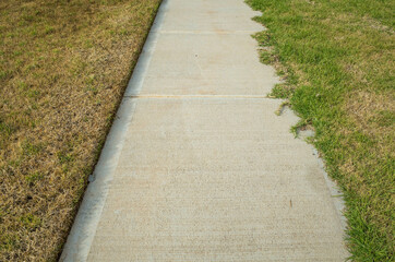 A concrete pedestrian footpath with a perfect lawn edge on one side and overgrown grass on the...