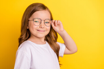 Profile side photo of young little girl happy positive smile confident hand touch eyeglasses isolated over yellow color background