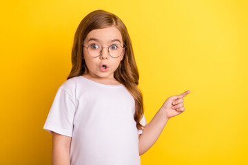 Photo of young little girl amazed shocked omg wow point finger empty space advertise direct isolated over yellow color background - obrazy, fototapety, plakaty