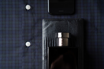 Casual style background. Male perfume bottle, leather purse, cellphone and shirt. Top view.