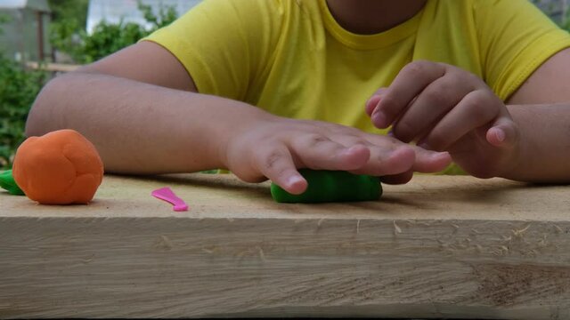 The child sculpts various figures on a wooden board from soft multi-colored plasticine. Close-up