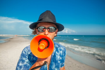 a man with a beard in a hat with glasses speaks into a loudspeaker in summer