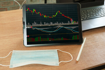 Stock market graph data analyzing in tablet and  Medical mask concept on table
