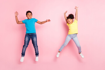 Full length body size view of two attractive cheerful kids jumping having fun isolated over pink pastel color background