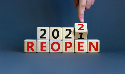 2022 reopen new year symbol. Businessman turns a wooden cube and changes words 'Reopen 2021' to...