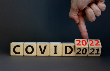 Symbol of covid-19 pandemic in 2022. Doctor turns wooden cubes and changes words 'covid 2021' to 'covid 2022'. Beautiful grey background, copy space. Medical, covid-19 pandemic in 2022 concept.