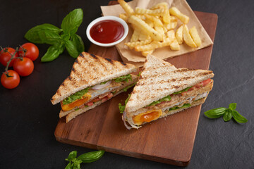 Fototapeta na wymiar Club-sandwich with french fries. Sandwich with bacon, fried egg. Grilled and pressed toast with bacon, fried egg, tomato and lettuce served on wooden cutting board.