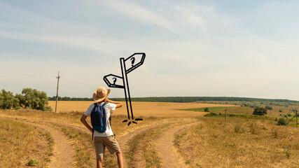 A young boy with a backpack stands at a fork in two roads at the road sign solving the problem of...