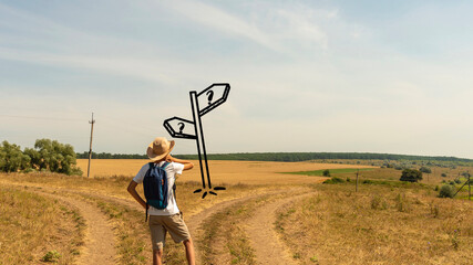 A young boy with a backpack stands at a fork in two roads at the road sign solving the problem of choosing the right path in life © rozaivn