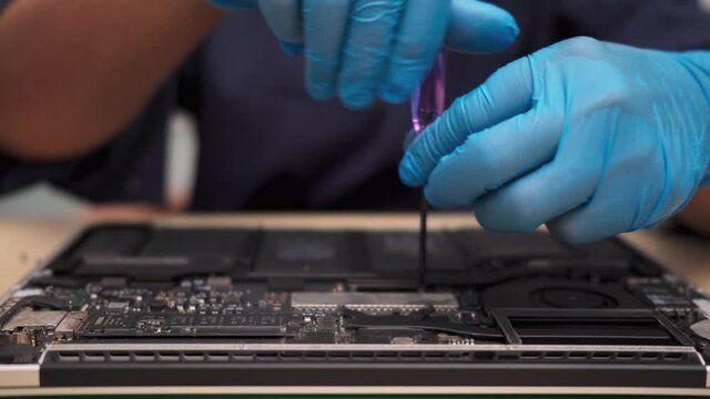 technician wearing rubber gloves is fixing and checking a broken notebook with a screwdriver.