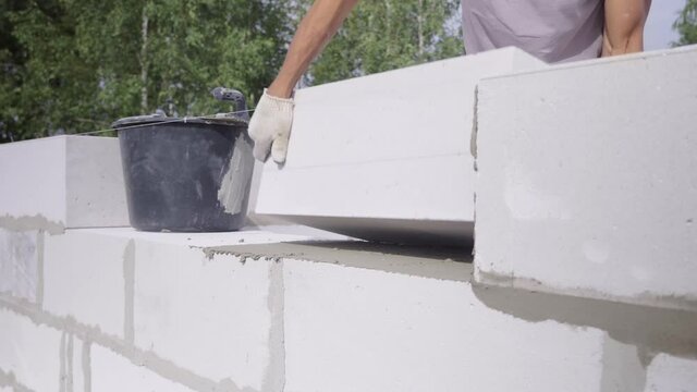 The hands of a bricklayer lay a wall of a white block close-up. A bricklayer Installs concrete blocks on a sunny day in summer. Contribution to the future and investment. business. Slow-motion action.